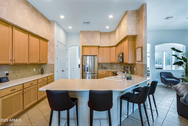 kitchen featuring a kitchen bar, sink, appliances with stainless steel finishes, light tile patterned floors, and light brown cabinetry