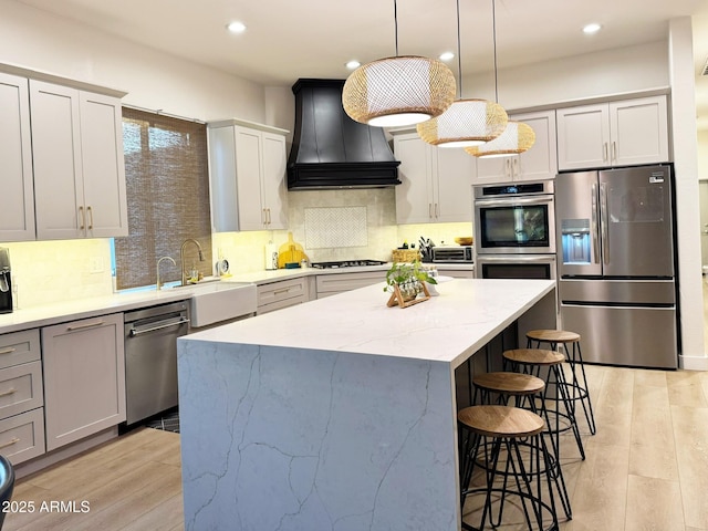 kitchen with stainless steel appliances, premium range hood, a breakfast bar, a kitchen island, and light wood finished floors