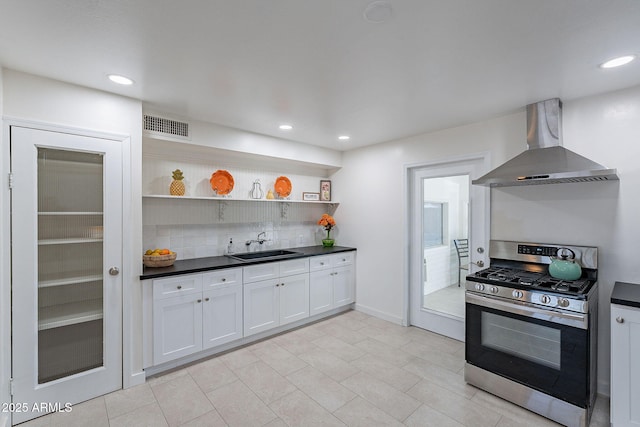 kitchen featuring wall chimney range hood, sink, stainless steel gas stove, backsplash, and white cabinets