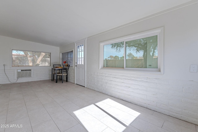 tiled spare room with lofted ceiling, brick wall, a wall mounted AC, and a wealth of natural light