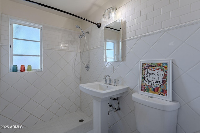 bathroom featuring tiled shower, toilet, sink, and tile walls