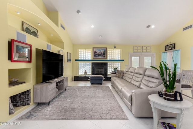 tiled living room with french doors, a tile fireplace, and vaulted ceiling