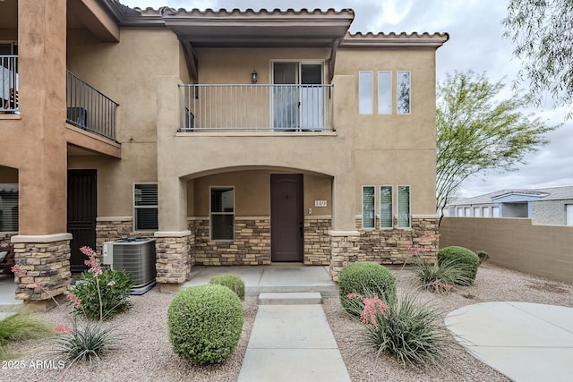 view of front facade featuring central AC, stone siding, stucco siding, and fence