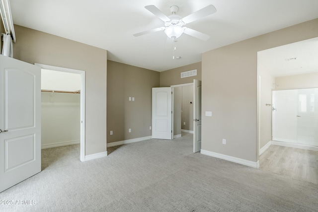 unfurnished bedroom with a walk in closet, light carpet, baseboards, and visible vents