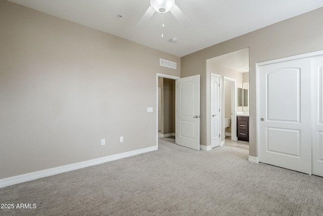 unfurnished bedroom featuring ensuite bathroom, light colored carpet, visible vents, ceiling fan, and baseboards