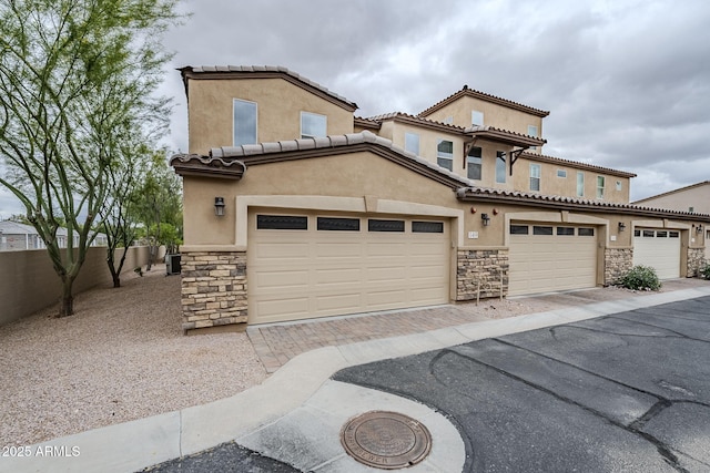 view of front of house with stucco siding, stone siding, and driveway