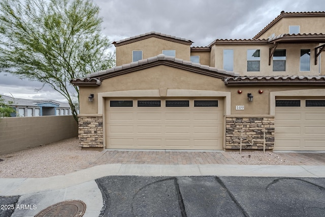 view of front of house with fence, stucco siding, decorative driveway, and stone siding