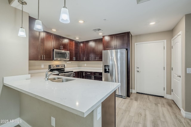 kitchen with light stone counters, light wood finished floors, a peninsula, and appliances with stainless steel finishes