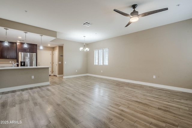 unfurnished living room featuring baseboards, visible vents, light wood-type flooring, and ceiling fan with notable chandelier