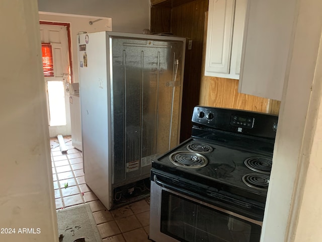 kitchen featuring fridge, black / electric stove, light tile patterned floors, and white cabinetry