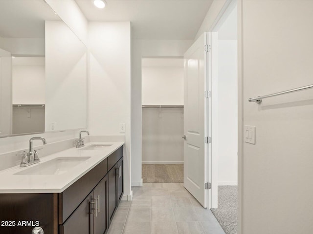 full bathroom featuring a walk in closet, a sink, baseboards, and double vanity