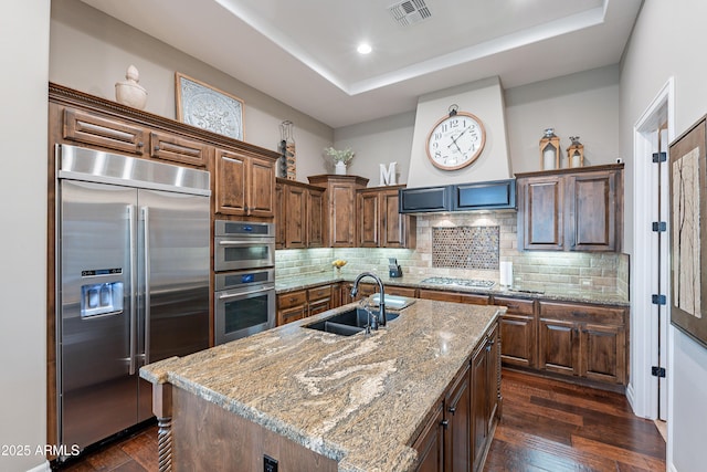 kitchen with stainless steel appliances, a sink, visible vents, dark wood-style floors, and a center island with sink