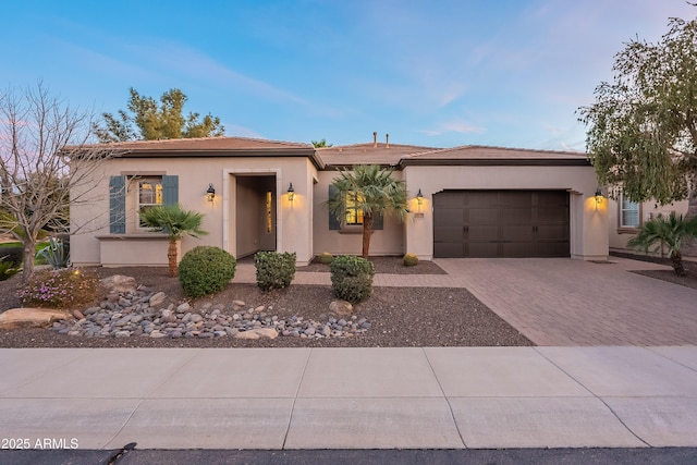 view of front of home featuring a tiled roof, decorative driveway, an attached garage, and stucco siding