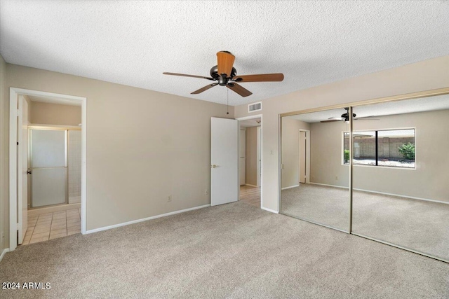 unfurnished bedroom featuring light carpet, a textured ceiling, a closet, and ceiling fan