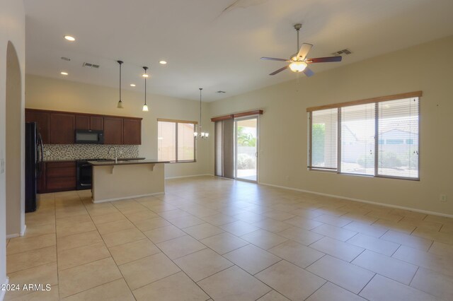 kitchen with decorative backsplash, a center island with sink, black appliances, a kitchen breakfast bar, and light tile patterned flooring