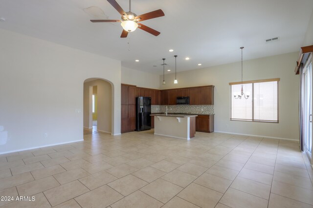 kitchen featuring backsplash, a kitchen island with sink, ceiling fan with notable chandelier, light tile patterned floors, and black appliances