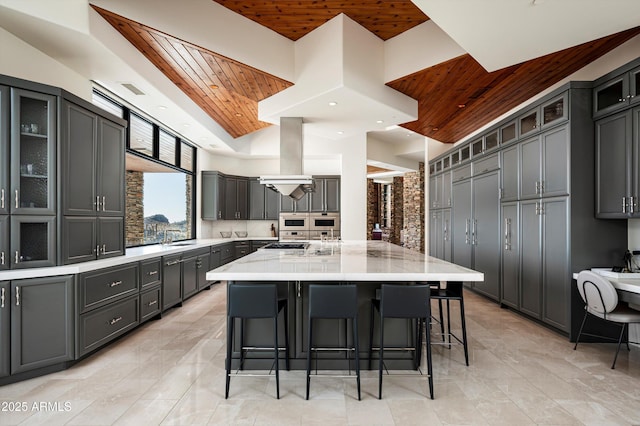 kitchen featuring wooden ceiling, a large island, a breakfast bar area, light stone countertops, and a sink