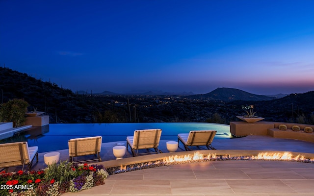 view of pool featuring a fire pit, an infinity pool, a mountain view, and a patio