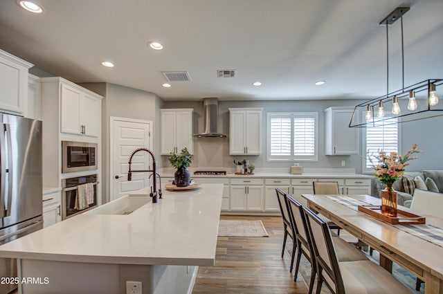 kitchen with appliances with stainless steel finishes, pendant lighting, wall chimney exhaust hood, sink, and white cabinetry