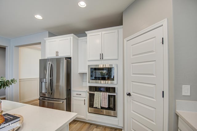 kitchen with stainless steel appliances, white cabinets, and light hardwood / wood-style flooring