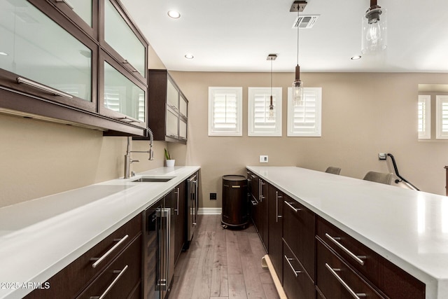 kitchen featuring wine cooler, sink, decorative light fixtures, dark brown cabinets, and light wood-type flooring