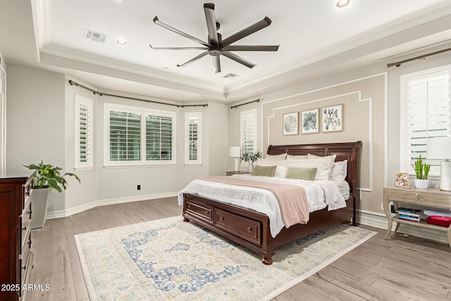 bedroom featuring multiple windows, crown molding, light hardwood / wood-style floors, and a tray ceiling