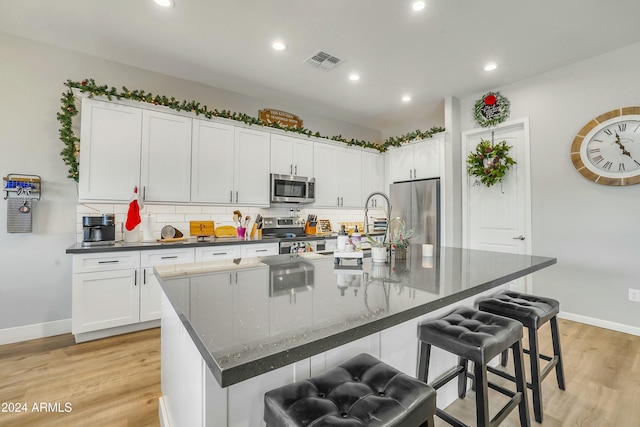 kitchen featuring white cabinets, light hardwood / wood-style floors, a large island with sink, and appliances with stainless steel finishes