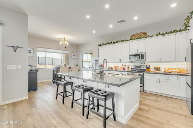 kitchen with white cabinetry, stainless steel appliances, a kitchen island with sink, and a breakfast bar area