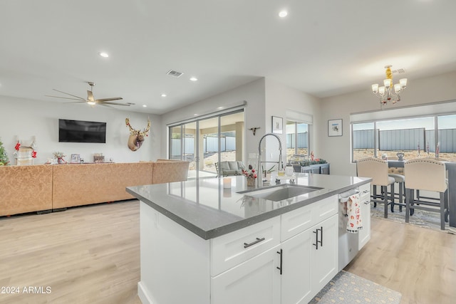 kitchen with ceiling fan with notable chandelier, sink, white cabinets, light hardwood / wood-style floors, and an island with sink