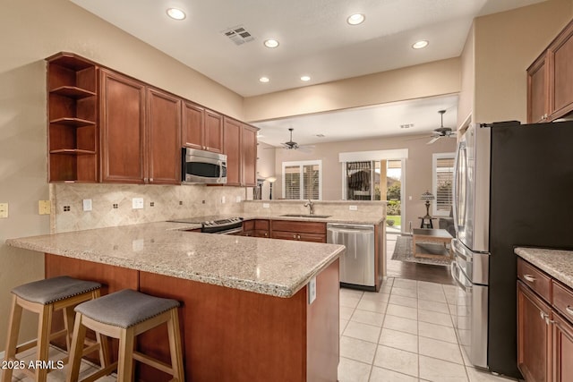 kitchen featuring appliances with stainless steel finishes, sink, a kitchen breakfast bar, kitchen peninsula, and light stone counters