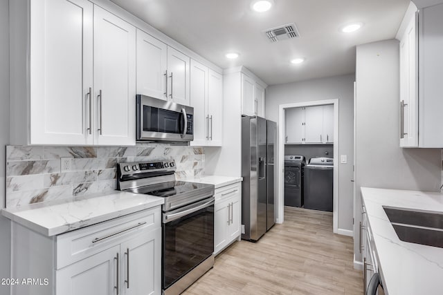 kitchen with white cabinets, appliances with stainless steel finishes, light stone countertops, light hardwood / wood-style floors, and washer and clothes dryer