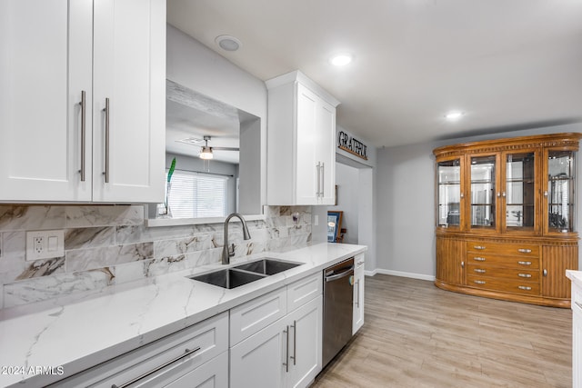 kitchen featuring dishwasher, backsplash, sink, white cabinetry, and light stone counters