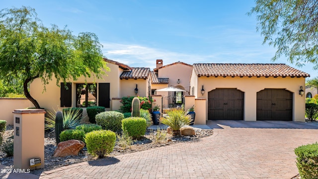 mediterranean / spanish-style home featuring a tiled roof, stucco siding, a chimney, decorative driveway, and a garage