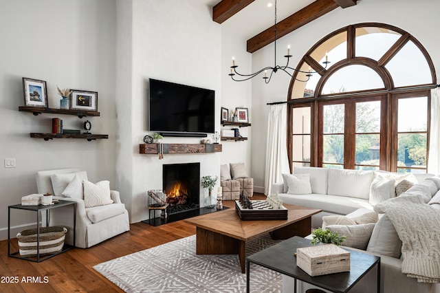 living area with beamed ceiling, a fireplace with flush hearth, wood-type flooring, a high ceiling, and baseboards