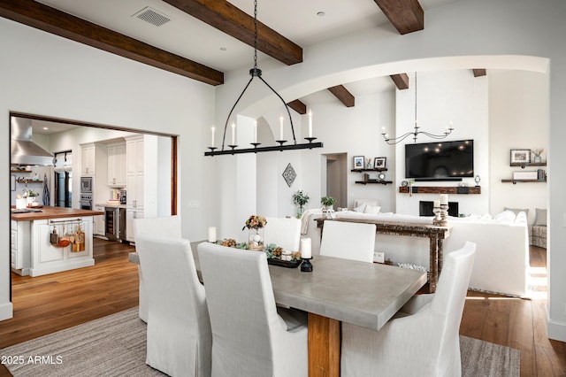 dining space featuring hardwood / wood-style floors, beverage cooler, visible vents, beamed ceiling, and a notable chandelier