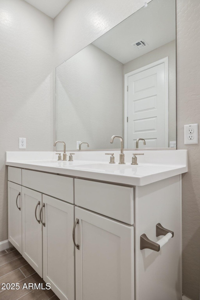 bathroom with a sink, double vanity, visible vents, and wood finish floors