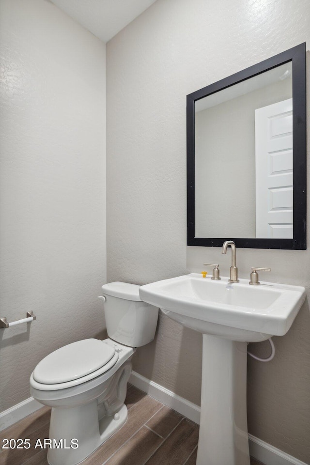 bathroom with a sink, toilet, baseboards, and wood tiled floor