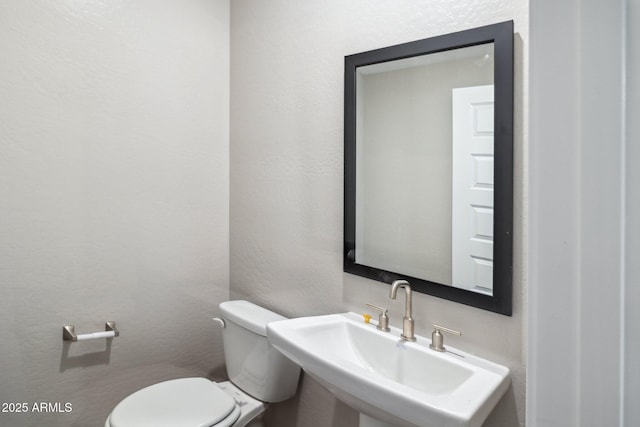 half bath featuring toilet, a textured wall, and a sink