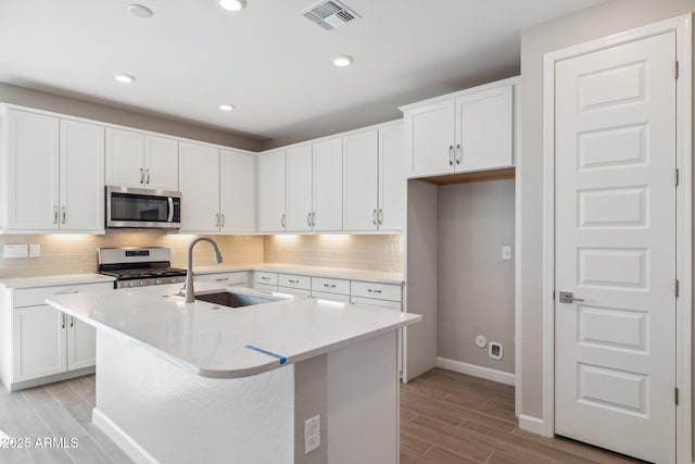 kitchen with visible vents, wood finish floors, a sink, decorative backsplash, and appliances with stainless steel finishes