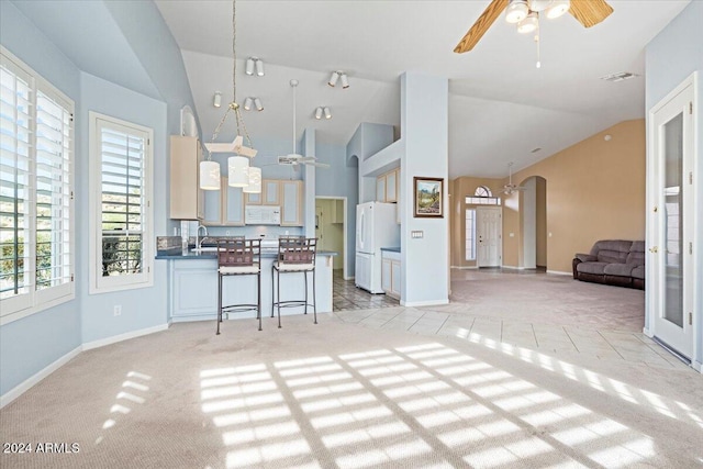 kitchen with white appliances, light colored carpet, hanging light fixtures, a kitchen breakfast bar, and ceiling fan