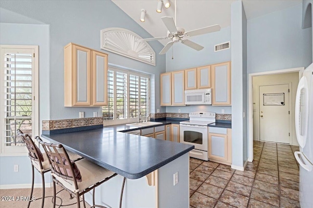 kitchen featuring sink, white appliances, high vaulted ceiling, light brown cabinetry, and kitchen peninsula