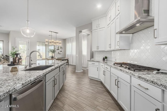 kitchen featuring white cabinetry, sink, wall chimney exhaust hood, hanging light fixtures, and stainless steel appliances