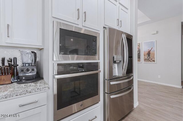 kitchen with light stone counters, white cabinetry, and stainless steel appliances