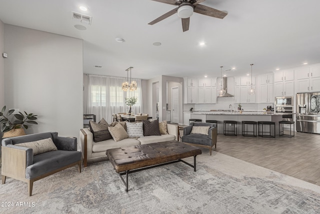 living room with ceiling fan with notable chandelier, light hardwood / wood-style floors, and sink