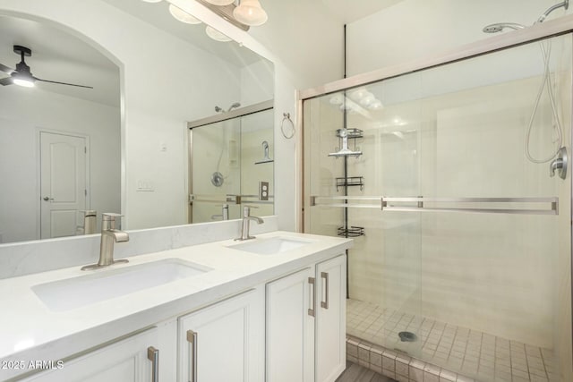 full bath with a sink, a shower stall, a ceiling fan, and double vanity