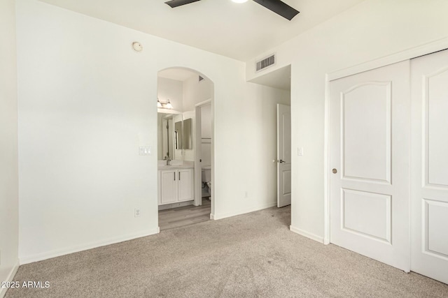 unfurnished bedroom featuring visible vents, light colored carpet, a closet, arched walkways, and a sink