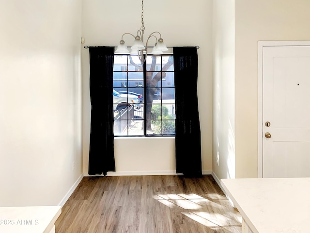 unfurnished dining area featuring light wood-style flooring, baseboards, and a chandelier