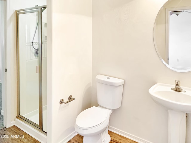 bathroom with a shower stall, baseboards, toilet, wood finished floors, and a sink