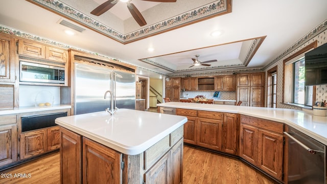 kitchen with built in appliances, a center island, ceiling fan, tasteful backsplash, and light hardwood / wood-style flooring