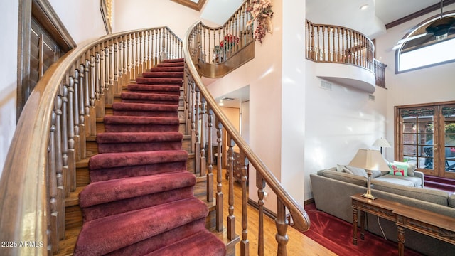 stairs featuring crown molding, a towering ceiling, and wood-type flooring